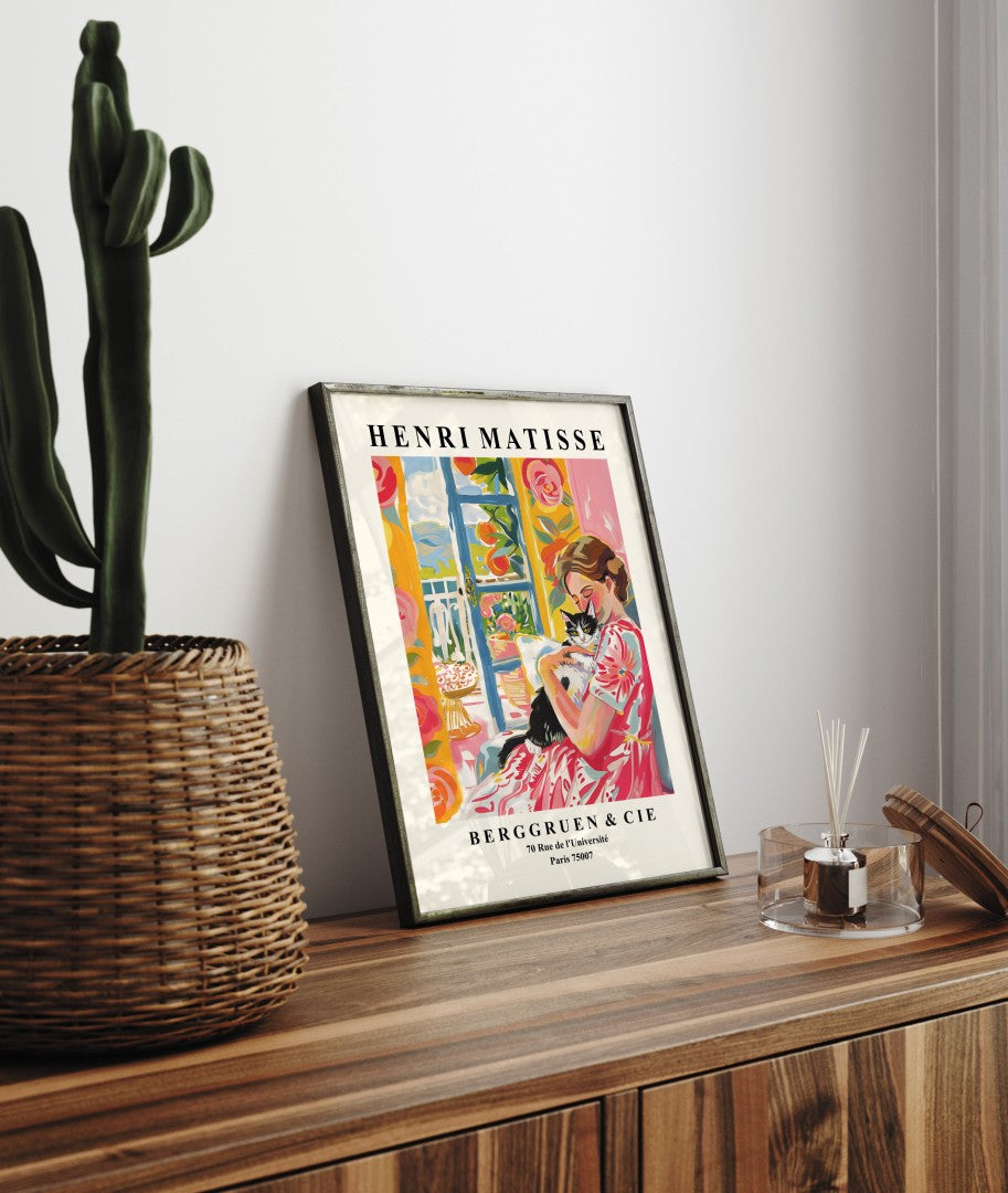 Framed artwork showing a woman with a cat in a sunlit interior.