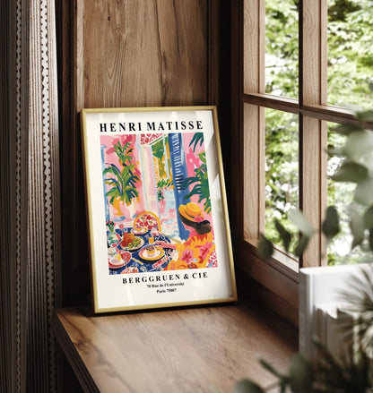 Framed artwork of a woman in a hat at a colorful outdoor café.