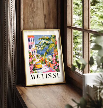 Framed artwork of a seaside village with flowers, palms, and a classic car.