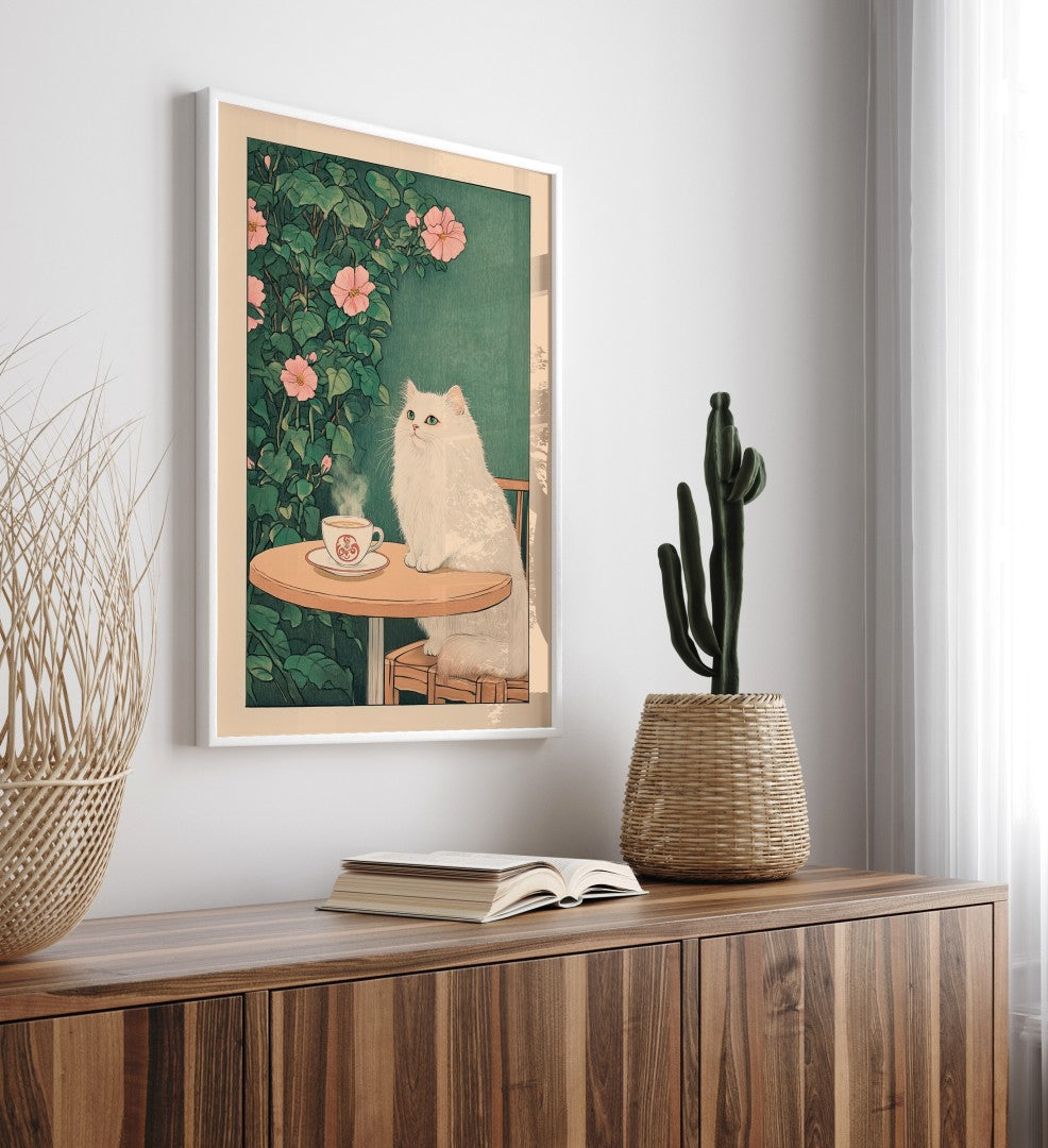 Framed artwork of a white cat by a table with a cup, placed on a wooden surface.